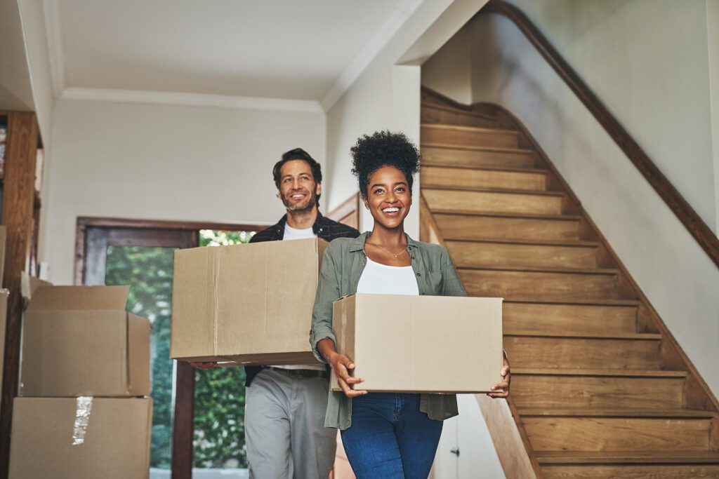 Happy couple, real estate and moving in new home with boxes for renovation, investment or relocation. Man and woman owner carrying box for property rent, mortgage loan or move together.